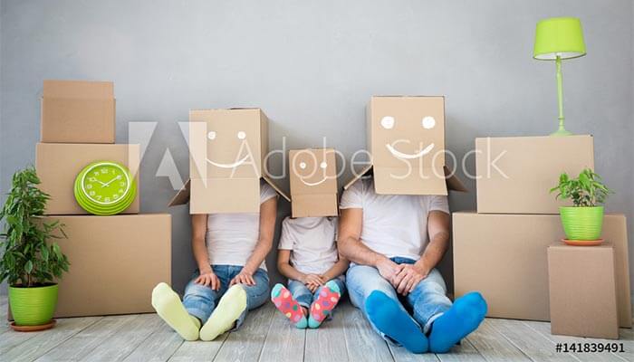 Eine Familie die am Boden sitzt mit Kartons auf dem Kopf